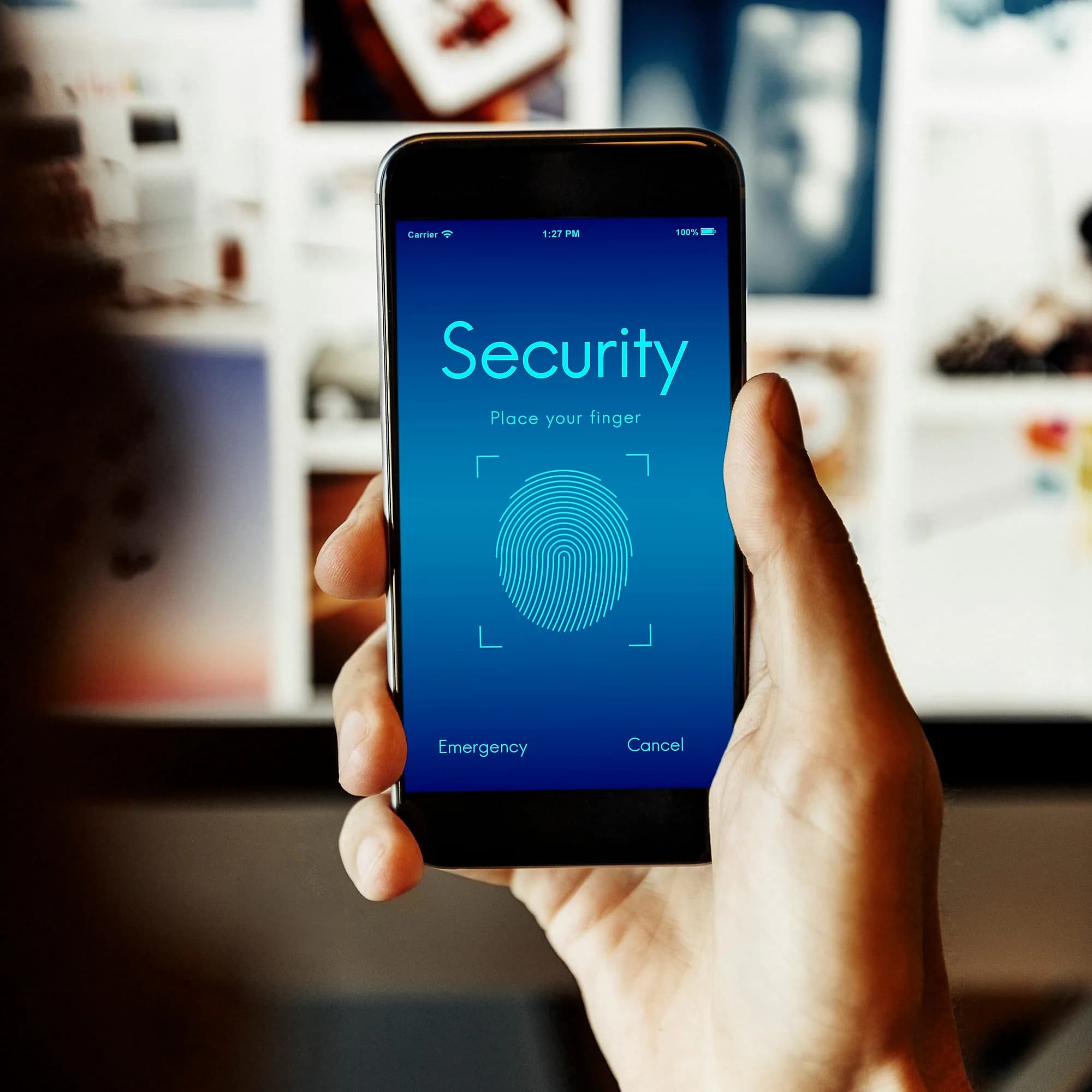 Hand holding a phone running a fingerprint security scan in front of a monitoring wall